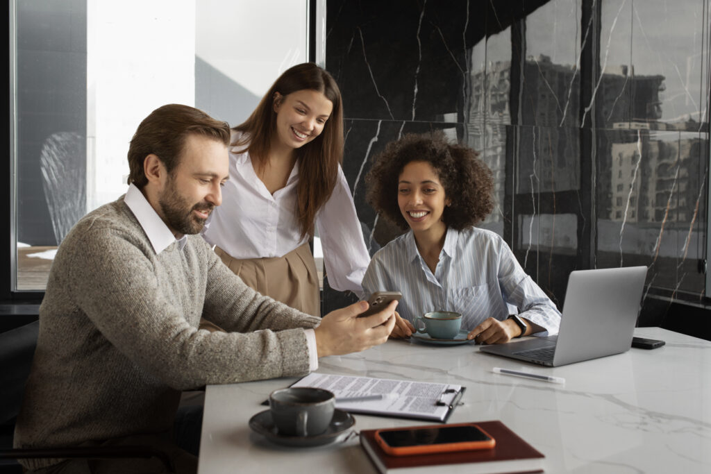 Three smiling coworkers having a discussion around a table with coffee, a laptop, and documents.