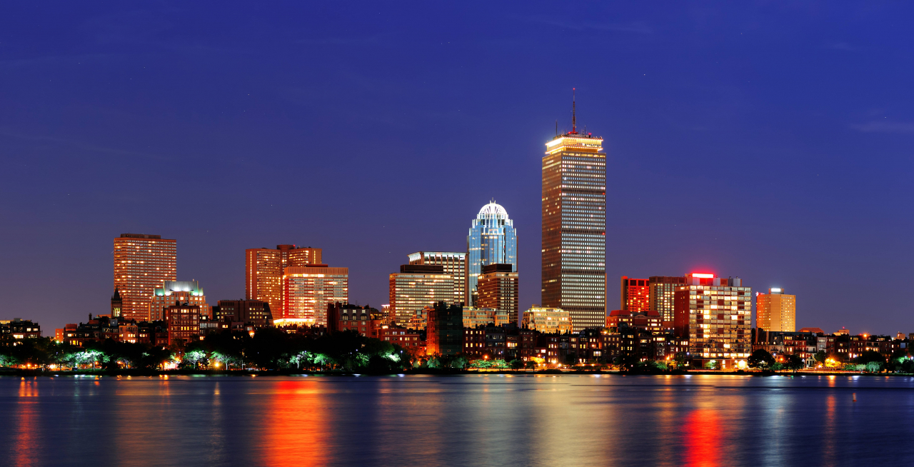 City skyline at night with illuminated skyscrapers reflecting on water.