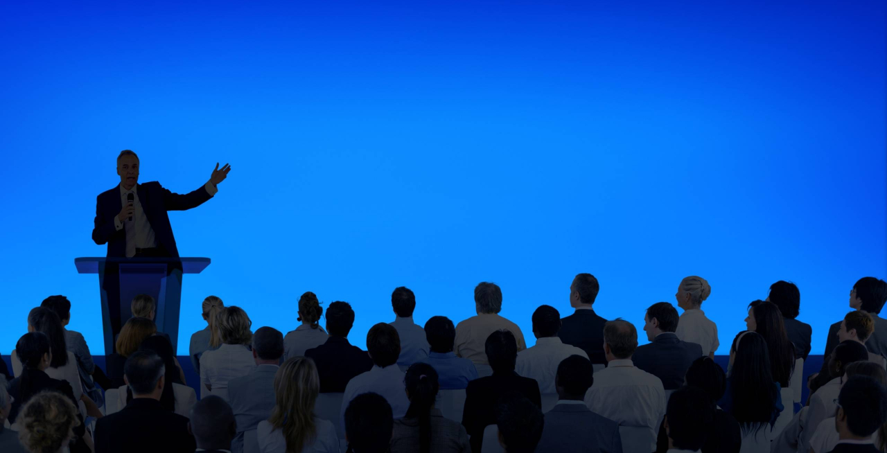 corporate-businessman-giving-presentation-large-audience-min