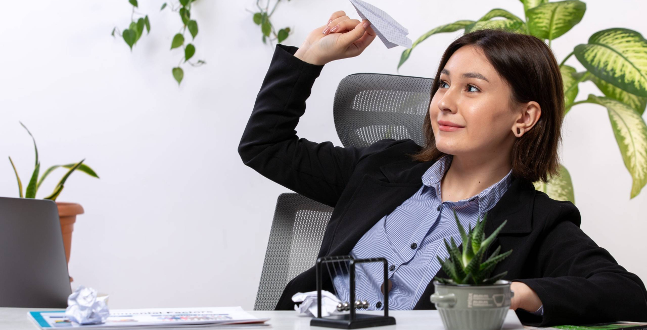 front-view-beautiful-young-businesswoman-black-jacket-blue-shirt-smiling-throwing-paper-planes-front-table-business-job-office-min