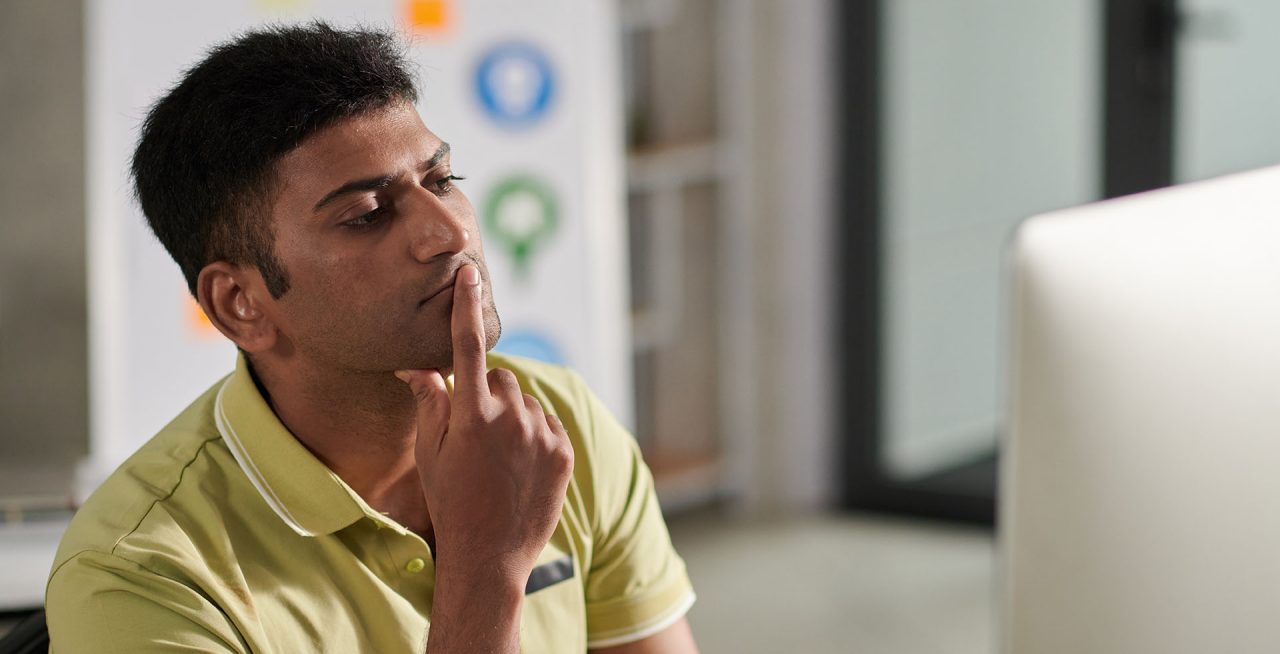 Portrait of pensive UX designer looking at computer screen deciding what to change in mockup